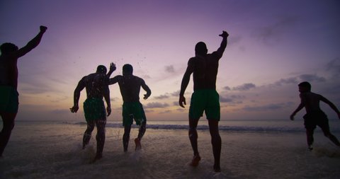 The young african happy carefree men friends are running towards the sea and having fun to splash a water on a sunset. Concept: lifestyle, holidays, happiness, vacation, friendship,freedom