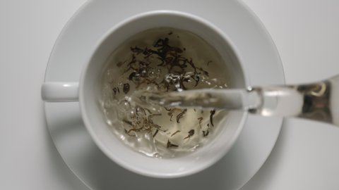 SLOW MOTION: Pouring Water Over The Black Tea Leaves In White Cup - Top view
