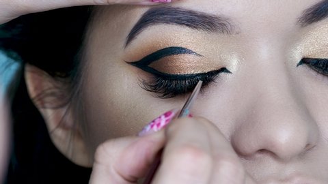 Beauty salon, makeup artist does evening makeup. Beautiful eyes with Golden eyeshadow. Eyebrow styling, Graphic bright arrows on the eyelids : vidéo de stock