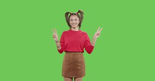 Young caucasian woman showing victory sign on green screen background. Girl having fun on chroma Key. 4k raw video footage slow motion 60 fps