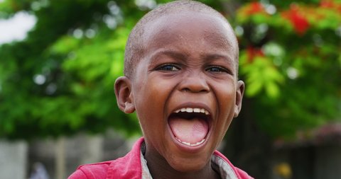 Authentic portrait of cute happy rural african toddler boy is smiling in camera on a village background. Concept: charity, people,life, happiness, authenticity