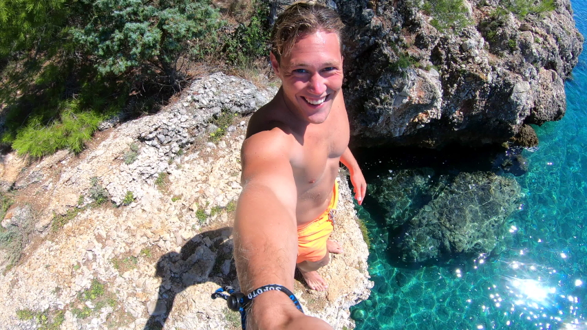 Young Man giving a thumbs up before jumping from a cliff with go-pro camera into a beautiful blue water on a sunny summer day in Croatia.  Royalty-Free Stock Footage #1047701965