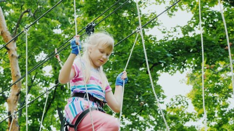 Purposeful child moves on ropes high on tree, uses safety rope