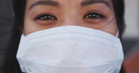 Portrait close up of a mixed race woman with dark hair out and about in the city streets during the day, wearing a face mask against air pollution and Coronavirus Covid19 , looking at camera