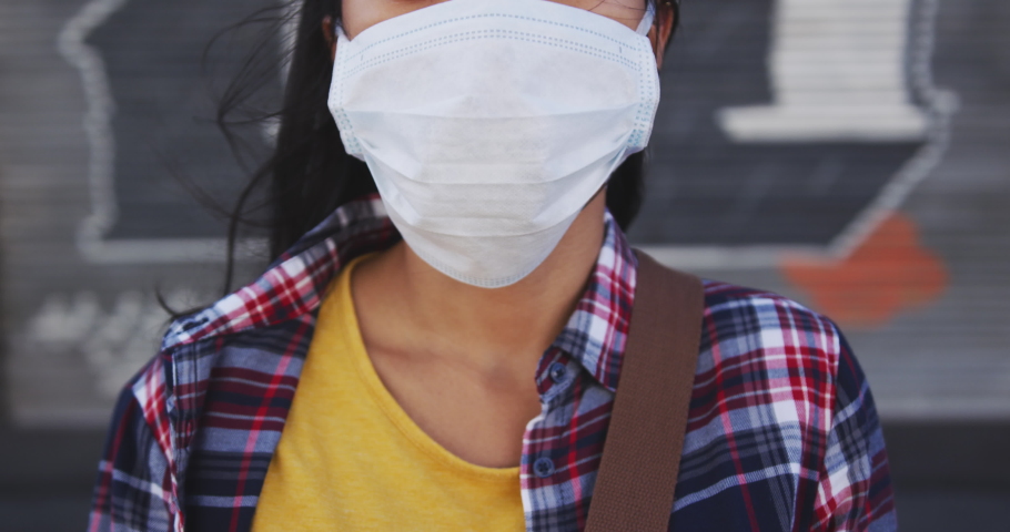 Portrait of a mixed race woman with dark hair out and about in the city streets during the day, wearing a face mask against air pollution and Coronavirus Covid19, looking at camera Royalty-Free Stock Footage #1047704782