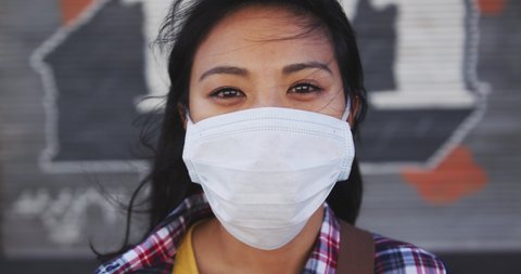 Portrait of a mixed race woman with dark hair out and about in the city streets during the day, wearing a face mask against air pollution and Coronavirus Covid19, looking at camera