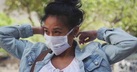 Side view of a mixed race woman with dark hair out and about in the city streets during the day, wearing a face mask against air pollution and Coronavirus Covid19, fastening her face mask