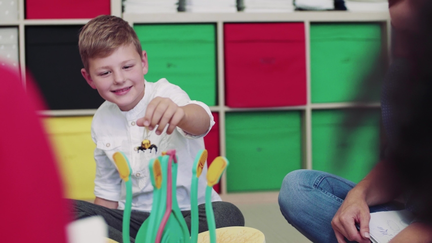A group of small school kids with teacher sitting on the floor in class, learning.