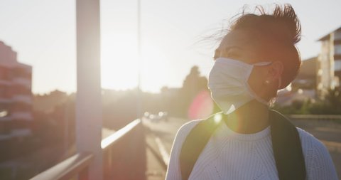 Front view of a mixed race woman with long dark hair out and about in the city streets during the day, wearing a face mask against air pollution and coronavirus Covid19, walking and using a smartphone