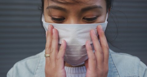 Portrait close up of a mixed race woman with dark hair out and about in the city streets during the day, wearing a face mask against air pollution and coronavirus Covid19, standing and looking at came