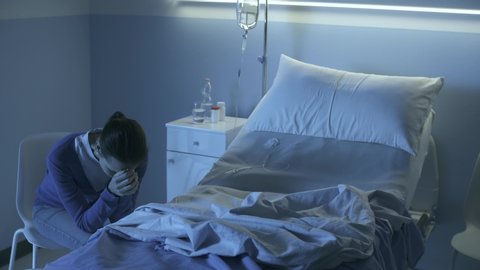 Sad lonely woman crying next to an empty hospital bed, terminal illness and mourning concept