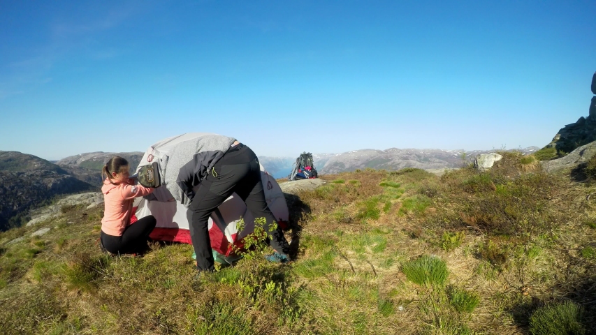 A young couple putting up the tent in the near Preikestolen, Norway. Wild camping in nature. Couple is having fun. Lysefjord in the back, going far inside the land. Freedom and adventure. 
