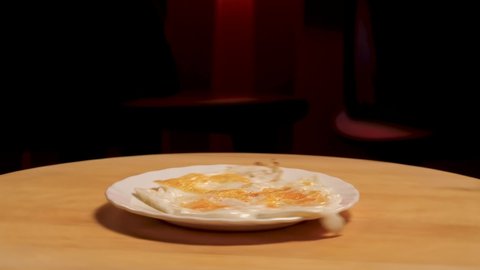 Fried egg on a plate rotating on a wooden board on dark room background. Stock footage. Close up of white glass plate with fried egg on it.
