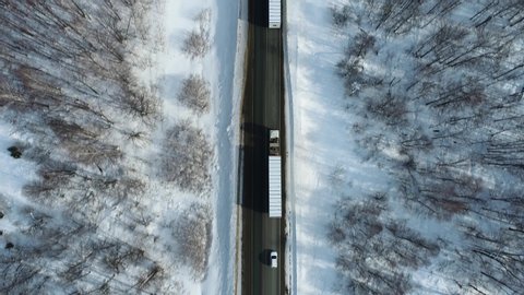 Two Semi Trucks with white trailer and cab driving, traveling alone on dense flat forest asphalt straight road, highway follow vehicle aerial mid shot at winter sunset. Freeway trucks traffic