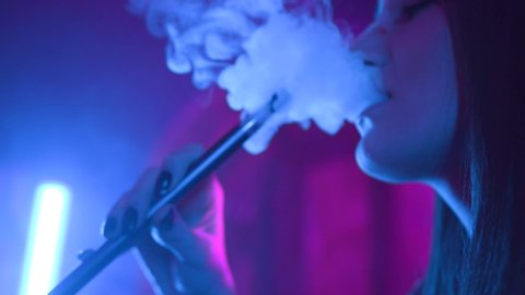 Close up view of young caucasian woman enjoying hookah at the bar feel happy young friendship communicate emotion shisha smoker male lounge handsome female vape beautiful attractive relax neon lights