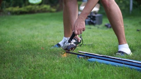 Young Handy Man Grinding Steel At Lawn In Garden - Medium Shot