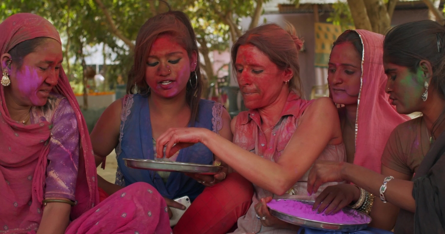 Indian women, traditional costume jewelry, smiling joyful laugh have fun taking photos selfie video with white western caucasian woman and check it on smart phone mobile outdoor in garden sitting Holi