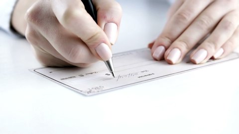 Female hand with pen filling a bank check. Paycheck concept. Payment by cheque