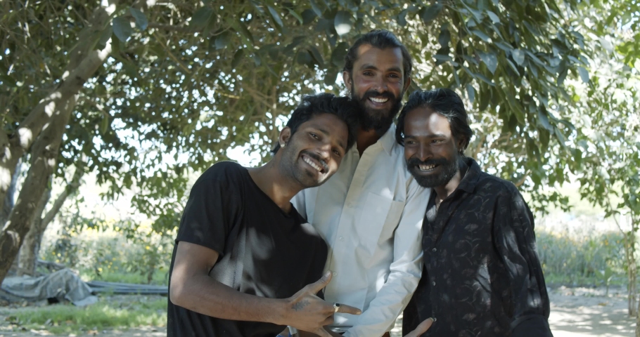 Three Indian male handsome good looking friends enjoying have a good time together as they hug toothy smile and pose together for photo video looking straight at camera taking selfies and reviewing