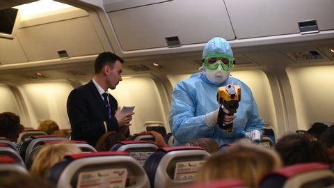 Moscow - March 04 2020. Temperature check on a corona virus at airplane. Medical official wearing infectious disease protection suite measure temperature of passengers inside the aircraft on arrival.