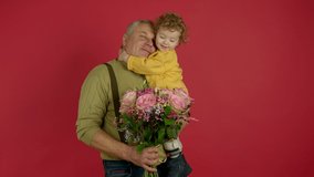 Smiling senior man holding flowers and kissing grandson