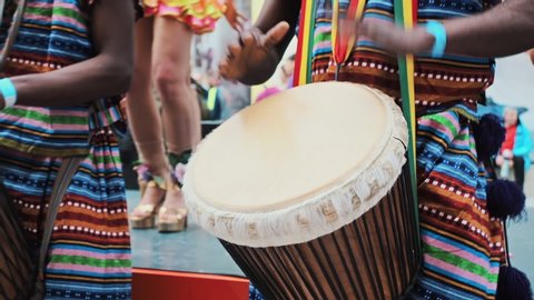 The celebration of the Brazilian carnival in Moscow. Musician beats rhythm on african drums. Black artists hit the drums with their hands. Girls dancers dance samba. Close-up African s hands playing