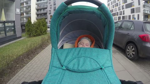Newborn baby girl sleep in her pushchair stroller cradle while walking between cars and flat houses in living district. Wide angle POV shot. 4K UHD.