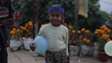 Kathmandu, Nepal - 17 November 2019: A cute little nepalese girl eating a cookie. Holding a balloon.