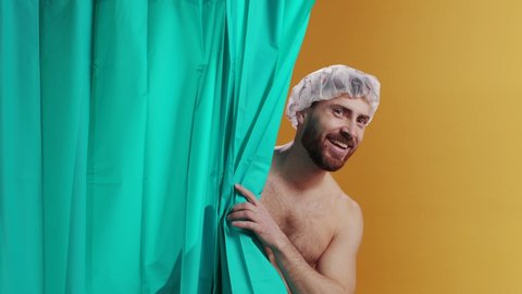 happy young bearded man wearing cap look behind shower curtain smile cheerful washing himself in the bathroom. Humor concept.