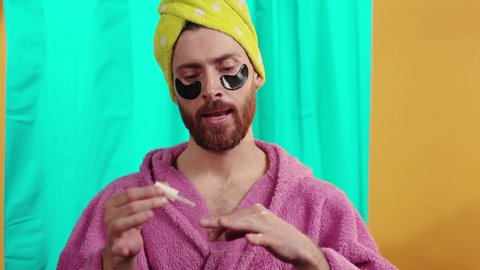 Portrait of bearded trans young man wearing pink bathrobe painting his hand nails singing alone smiling taking shower in the bathroom at home.