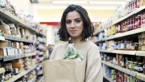 Young woman with paper bag in supermarket. Attractive young woman holding shopping bag and smiling at camera in grocery store. Shopping concept