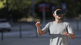 Young man using VR headset on street. Handsome smiling young man using virtual reality headset and touching air while standing outdoors. Technology concept