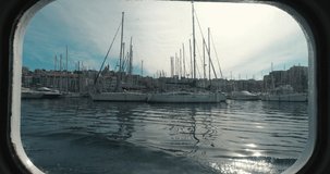 This stock video captures a POV look outside of a window of a boat, showcasing a scene of moored boats as it passes by.

