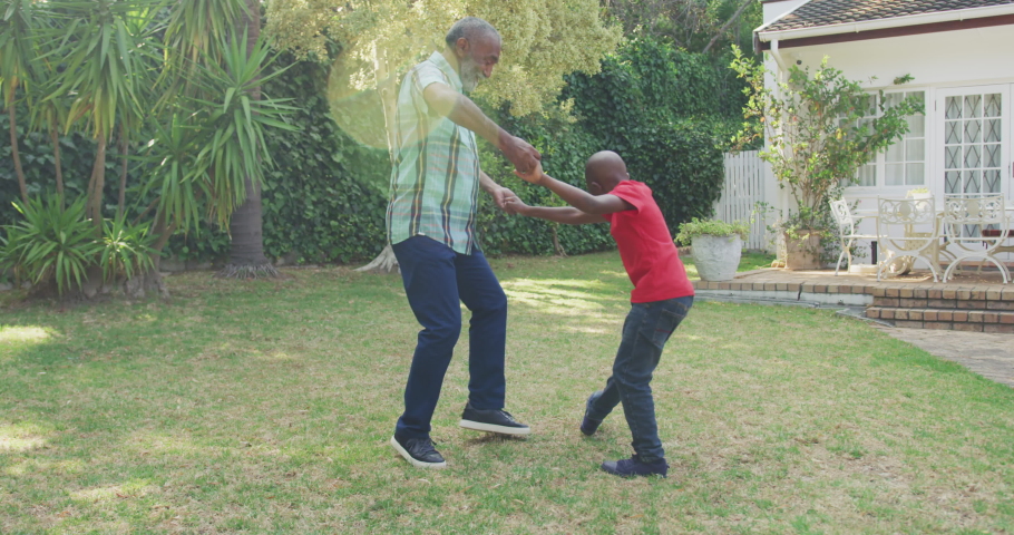 Side view of a senior mixed race man having a good time in a garden, holding hands and dancing with his son, on a sunny day, in slow motion