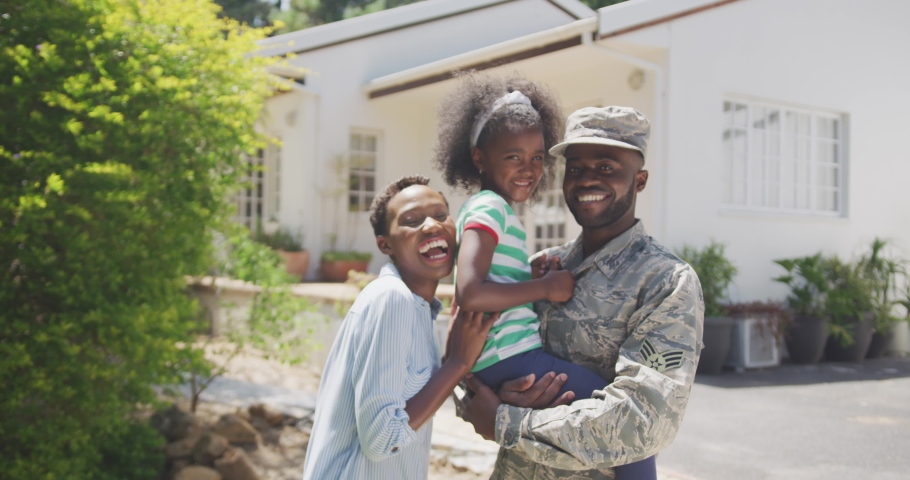 Side view of an African American family enjoying time in the garden, a man is wearing military uniform, holding up his daughter, looking at the camera, on a sunny day, in slow motion