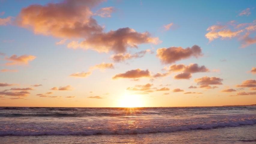 Light orange sunset in the ocean beach background. The best beach sunset in the world. Beautiful summer evening cloudy sun sunset landscape over sea water and waves beat against the sandy beach.