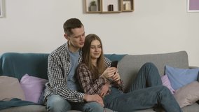 Smiling couple in checkered shirts using smartphone on sofa
