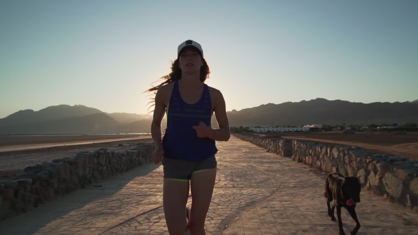 Slim girl jogging with her dog at pavement road at sunrise rapid slow motion