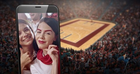 A phone with video of cheering fans on the screen is placed in front of professional basketball stadium. Stadium is made in 3D.