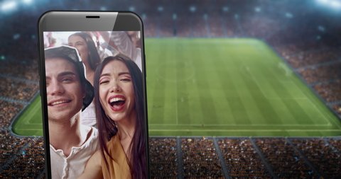 A phone with video of cheering fans on the screen is placed in front of professional soccer stadium. Stadium is made in 3D.