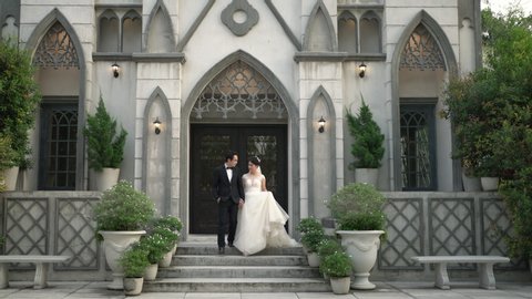Asian bride and groom walking together holding hands out of the church. Wedding couple in love. Handheld shot, Real life