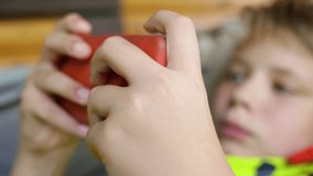 Closeup view of white kid playing online video games using smartphone. Focus in foreground at hands holding mobile cell, blurry face of young boy.