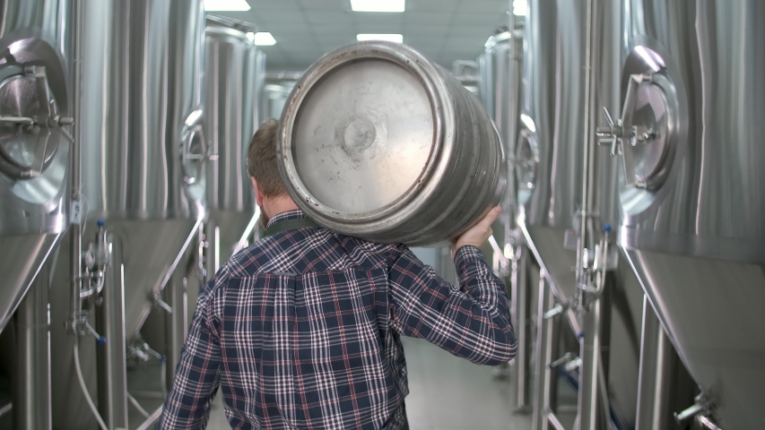 A working male brewer carries a keg filled with beer as he passes beer tanks. close-up. back view Royalty-Free Stock Footage #1047821836