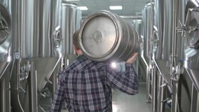 A working male brewer carries a keg filled with beer as he passes beer tanks. close-up. back view - Powered by Shutterstock - Get 15% off with code: PIKWIZARD15