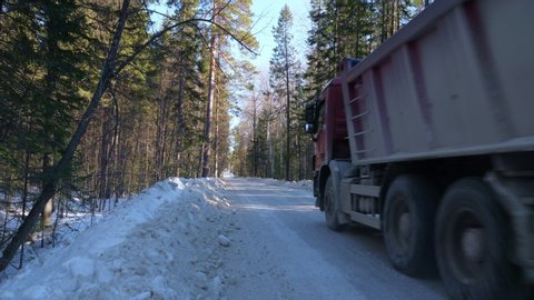 A truck carrying ore rides along a narrow winter forest road. The concept of labor and heavy industry