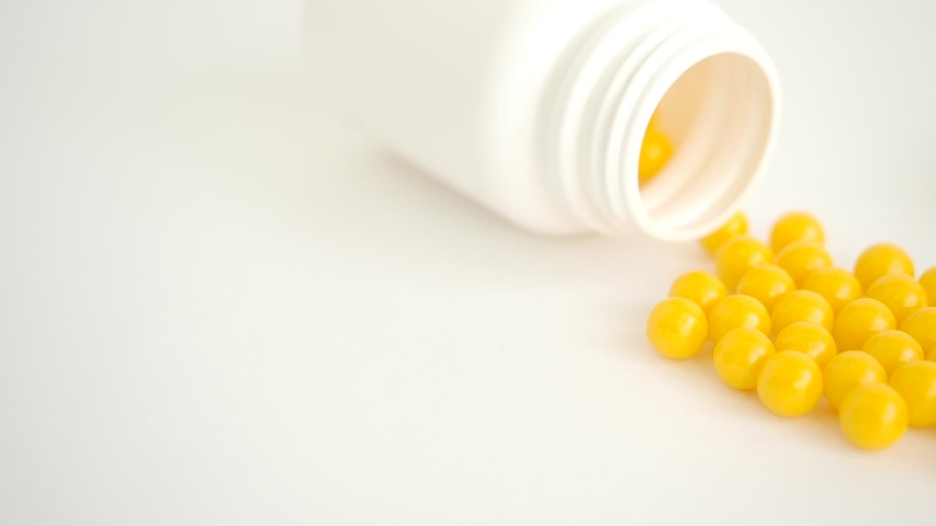 Vitamins. Antiviral drug tablets. Round yellow healthy pills and pill bottle on white background. Slow motion. Close-up