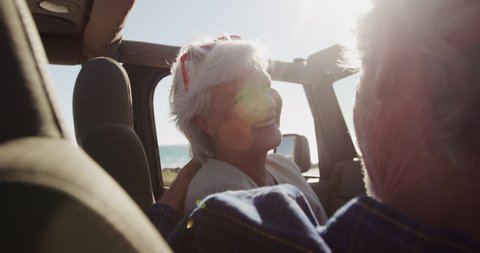 Over the shoulder view close up of a senior Caucasian couple sitting in their car during a road trip, driving to the beach in the sun, the man at the wheel, looking at each other in slow motion