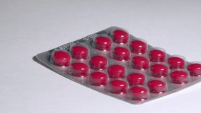 Red color pills in a blister fall down on a white background. Slow motion close-up view - Powered by Shutterstock - Get 15% off with code: PIKWIZARD15