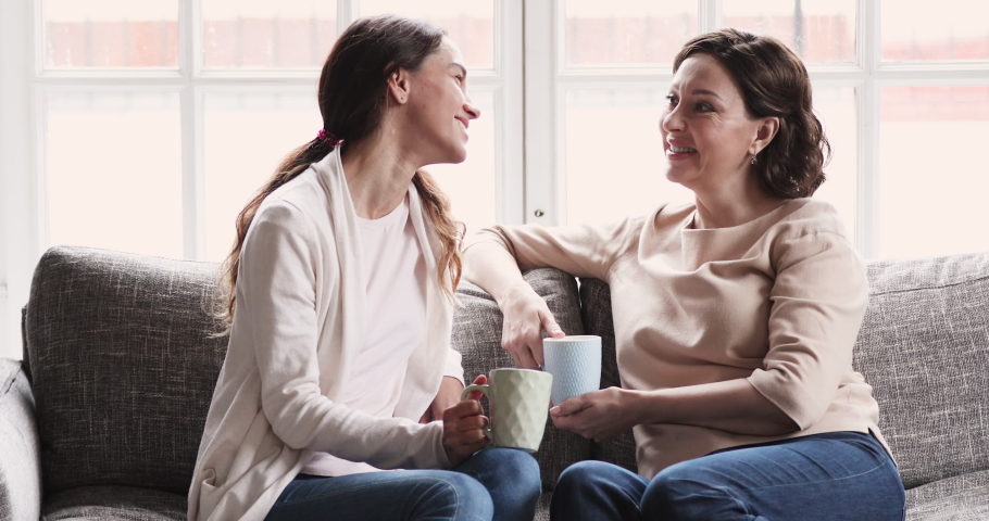 Relaxed middle aged mature old mother and young adult daughter talk drink tea on sofa. Happy 2 two generation women family chatting. Mom and grown child enjoy trust friendly honest conversation Royalty-Free Stock Footage #1047837493
