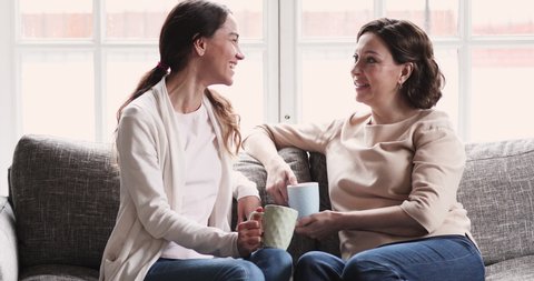 Relaxed middle aged mature old mother and young adult daughter talk drink tea on sofa. Happy 2 two generation women family chatting. Mom and grown child enjoy trust friendly honest conversation